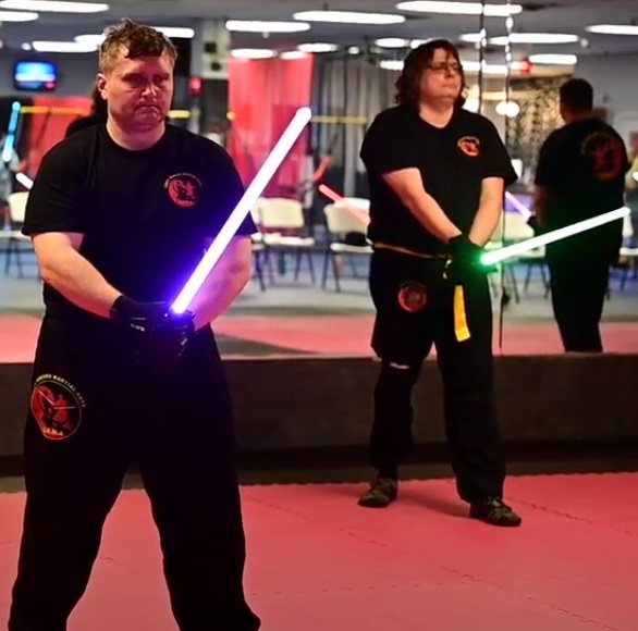 Two adult LSTA students in guard stance with lit sabers on the academy floor