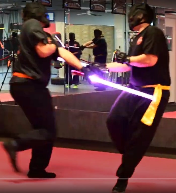 Two adult LSTA students in headgear sparring with lit sabers